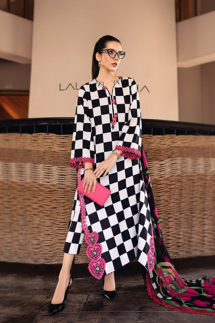 A model wears a black and white checkered three-piece suit set from M. Prints, featuring a printed lawn shirt, printed cambric trouser, and printed voile dupatta with pink floral embroidery.